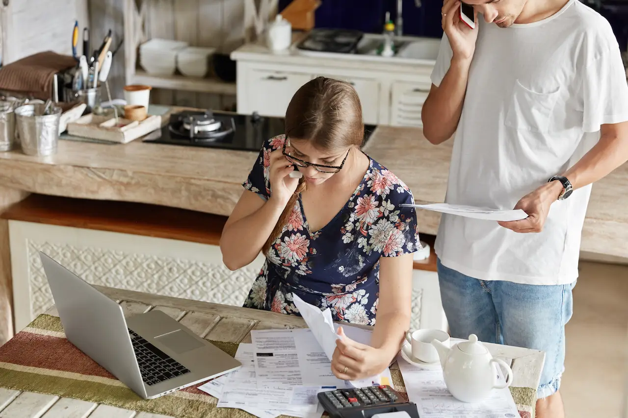 Couple reviewing household bills and managing budget with calculator and laptop at kitchen table
