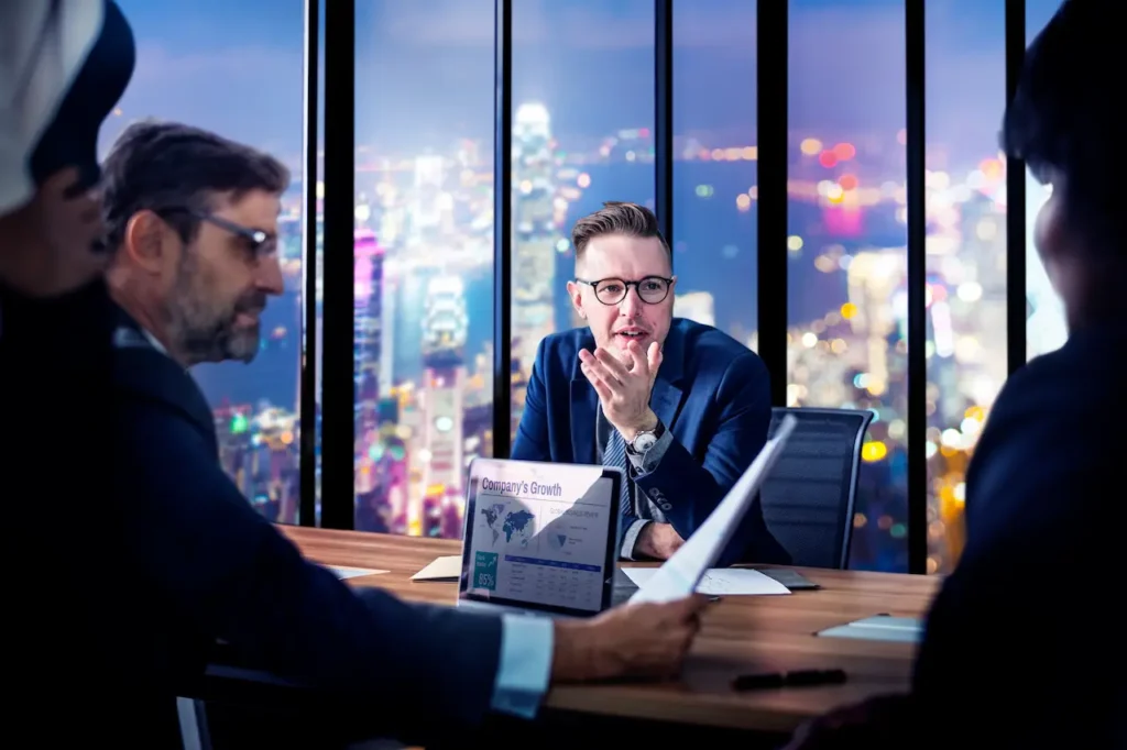 Business executives discussing company growth strategy during night office meeting with city skyline view
