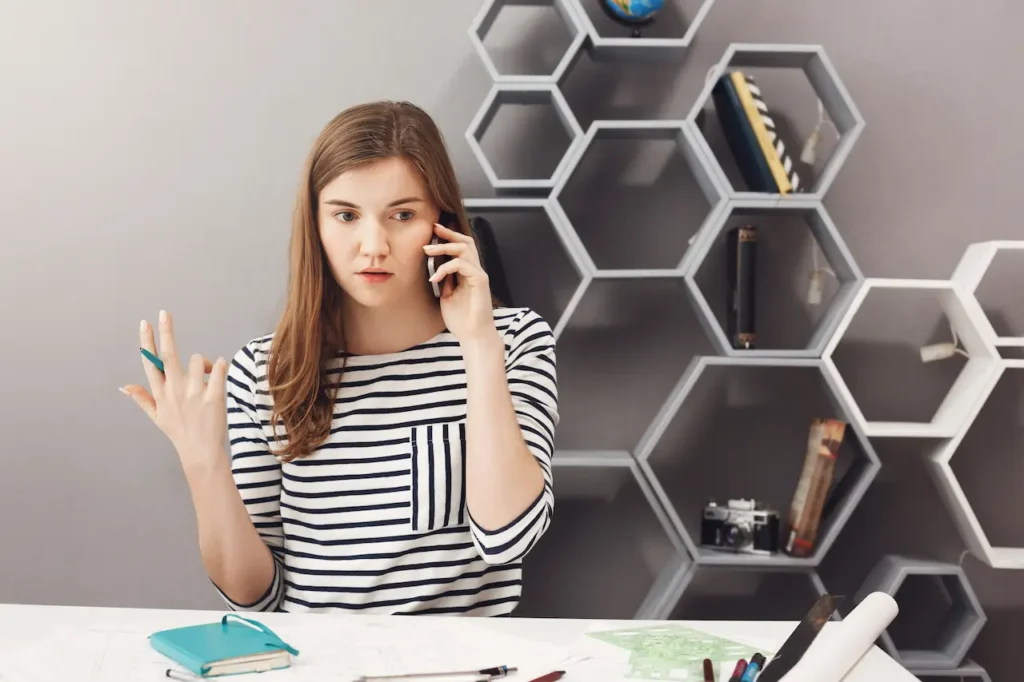 Young woman at desk talking on phone and gesturing while discussing a business matter