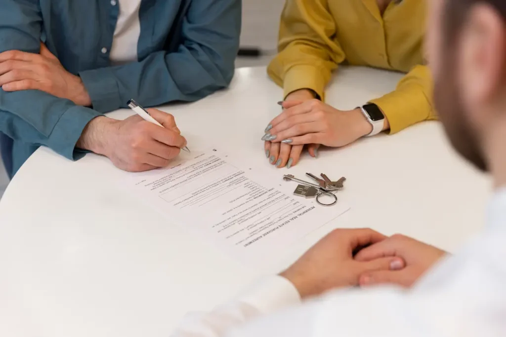 Couple signing real estate contract with house keys on table during property purchase meeting